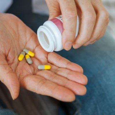 A close up photo of a hand pouring yellow and brown tablets from a white plastic pill bottle onto an open palm.